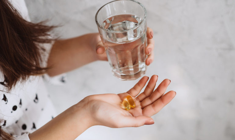 Woman holding vitamin D supplements in 1 hand and a glass of water in the other hand.
