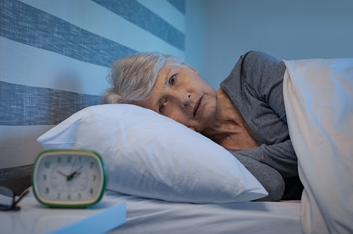 Older woman lying in bed staring at clock that reads 1 am.