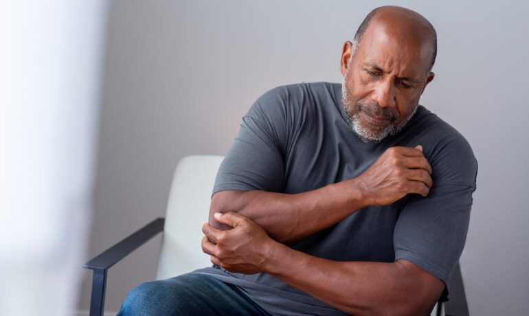 Older gentleman holding elbow in pain due to RA flare-up.